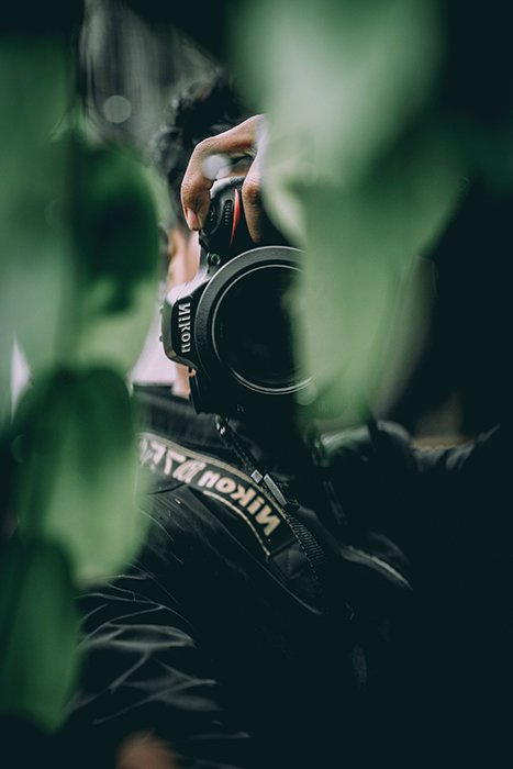 A photographer shooting through green leaves with a Nikon DSLR