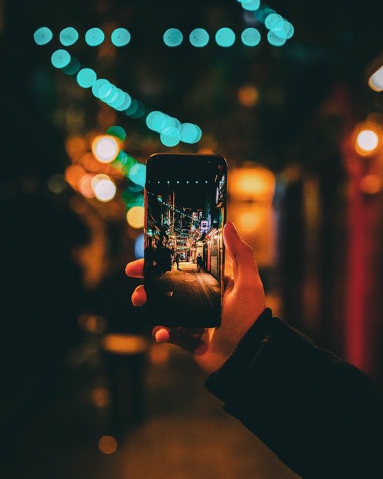 A hand holding a smartphone to naturally frame a night street photo using a wide and shallow depth of field together