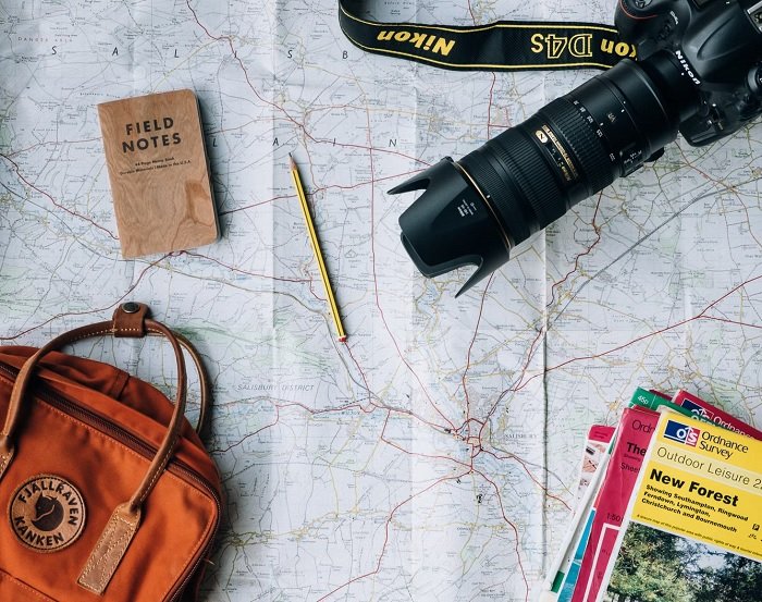 A large map laid out with a backpack, notepad, pencil, and camera on top.