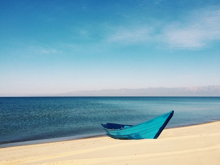 Blue boat on a sandy beach next to a still blue ocean