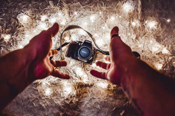 Hands reaching for a Nikon camera against a lit background