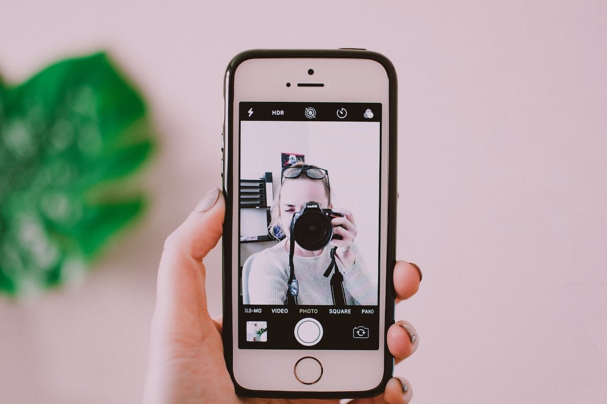 A selfie of a photographer taking a picture with a camera captured with a cell phone